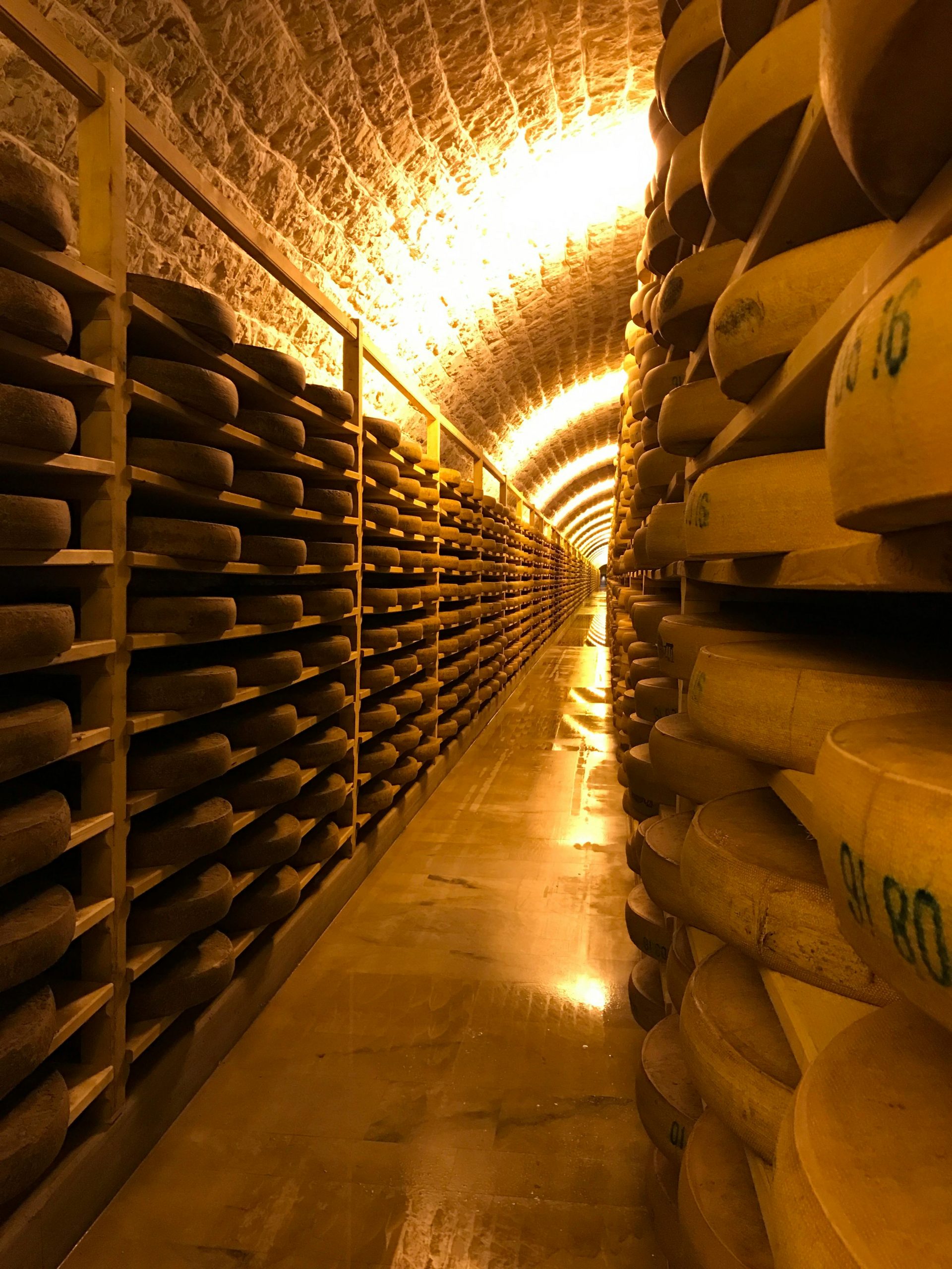 Services Rows of cheese aging on wooden shelves in a dimly lit storage room.